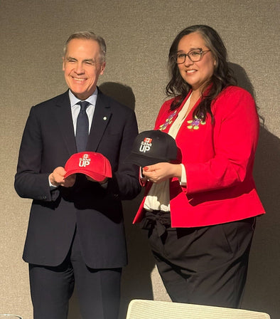 Prime Minister Mark Carney holding an Elbows Up Hat by Custom TShirts Canada
